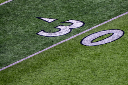 An American football field detail of white chalk drawn lines. 30 yard line