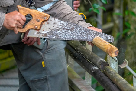 A man using a hand saw to cut wood.