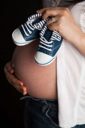 Pregnant woman holding a pair of baby shoes on her bellyの写真素材