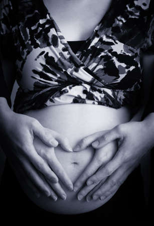 Pregnant woman making heart shape with hands over her stomachの写真素材