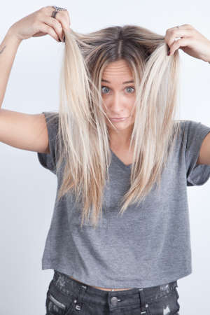 Portrait of a young blond woman playing with her hair against a white backgroundの写真素材