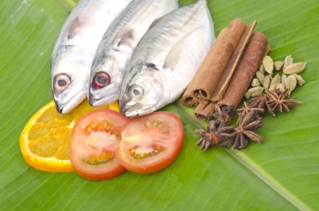 Close up of fresh fish decorated with lemon, tomato and spices stacked on banana leaf.の写真素材