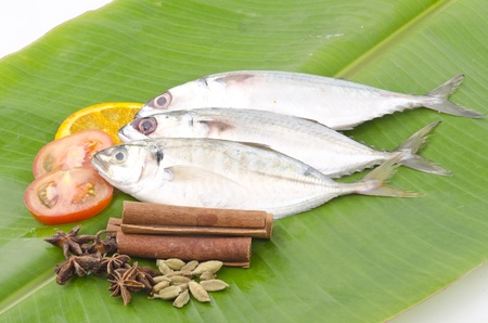 Fresh fish decorated with lemon, tomato and spices stacked on banana leaf.の写真素材