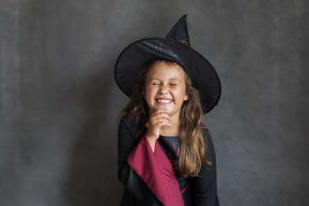 Happy girl in halloween witch costume on gray background