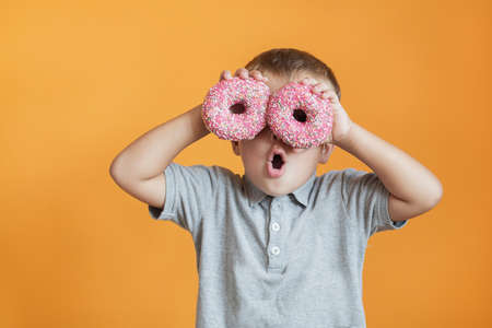 Happy boy with two donats on orange background