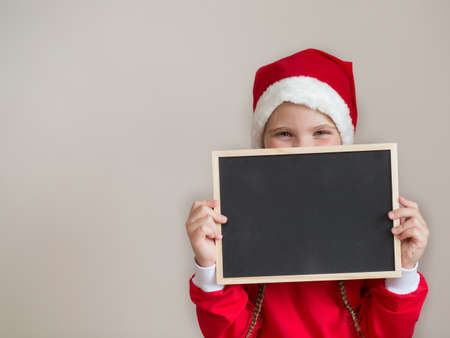 Happy girl in santa costume with black desk on light gray backgroundの写真素材