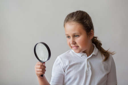 Little girl with magnifier on gray backgroundの写真素材