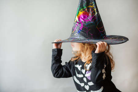 Toddler girl in halloween witch hat on her eyes on gray backgroundの写真素材