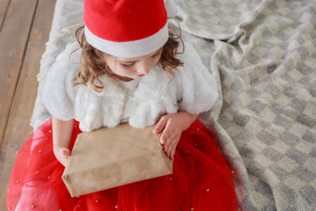 Little girl in santa costume with gift seating on the bedの写真素材