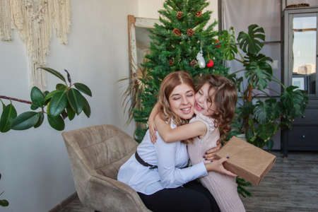 Mother and daughter sittig near Christmas tree with gift
