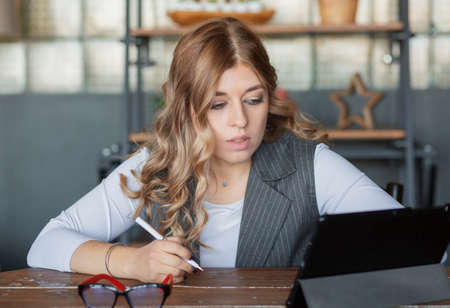 Blonde European businesswoman sitting with tablet and glasses