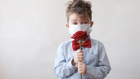 Cute little boy in bow tie with red rose and face mask valentine day.の写真素材