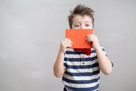 Cute boy in bow tie with red envelope near face. valentine day.の写真素材