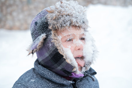 Crazy excited little cute boy in winter hat with snowy faceの写真素材