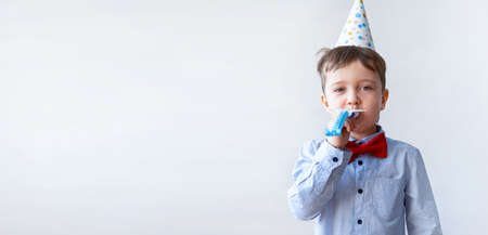 Cute little boy in red bowtie with party hat blow party horn. Birthday party.の写真素材