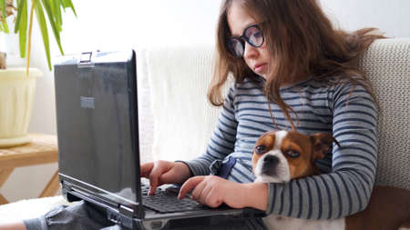 little cute caucasian girl in glasses study in laptop with dogの写真素材