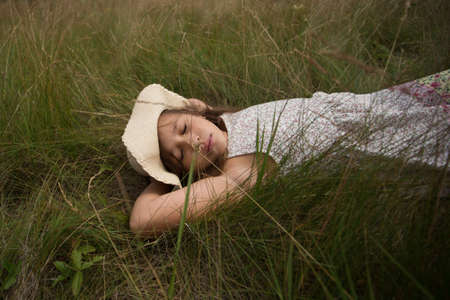 Little cute girl lying in summer field in hat and dress. Summer mood.