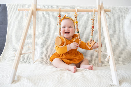 exited little baby girl plays with wooden toy toddler trainer sitting on couch