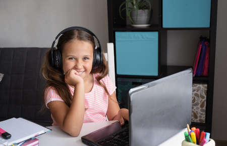 Happy caucasian girl using laptop with headphones studying at homeの写真素材