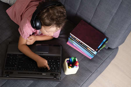 Cute caucasian boy using laptop and headphones studying at home