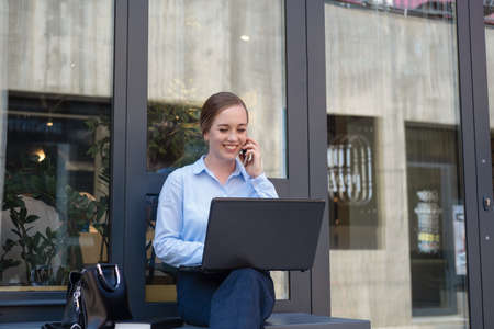 Portrait of happy business young woman, smiling while talk on phone and work with laptop