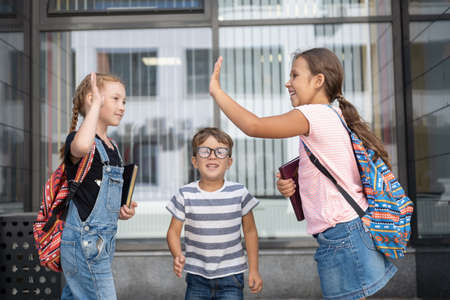 Three kids with backpack stand and talk together and give fiveの写真素材