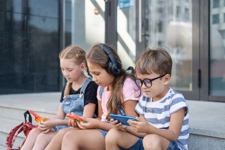 Three kids with backpack sit and play popit and phoneの写真素材