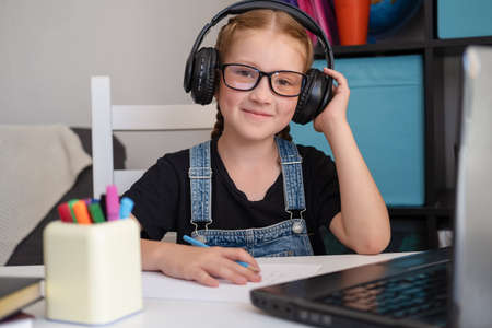 cute happy caucasian redhead girl in eyeglasses with headphones and laptop studying at homeの写真素材