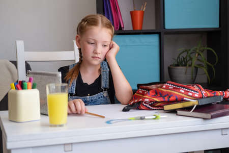 Cute sad redhead girl packing backpack, preparing for schoolの写真素材