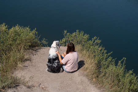 Woman sit with australian shepherd dog on river bank outdoor.の写真素材