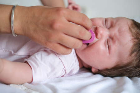 mothers hand give nipple to little crying baby girl. Happy familyの写真素材