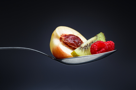 raspberries, peach and kiwi on curved spoon with reflection on gradient backgroundの写真素材