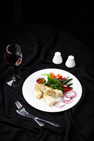 Chicken rolls with vegetables on white plate near glass of wineの写真素材