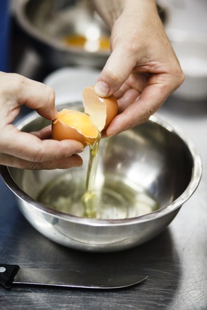 The chef breaks egg in a steel cup on professional kitchenの写真素材
