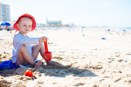 Adorable little girls sitting on a sand and looking away on the beach. Horizontal outdoors shot.の写真素材