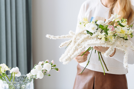 A girl florist makes a bouquet on a white tableの写真素材
