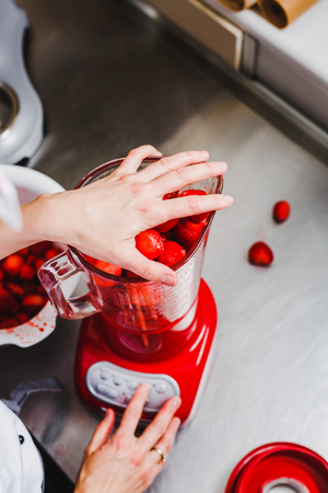Woman grind fresh strawberries in a red blenderの写真素材