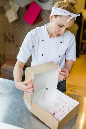 Woman wraps marshmallows in a cardboard box in a professional kitchenの写真素材
