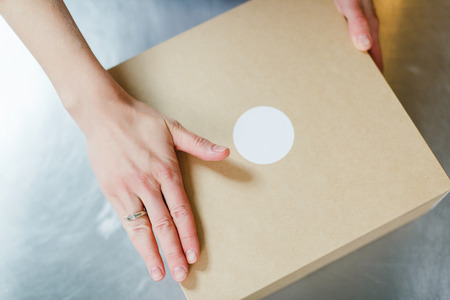 Female hands hold a cardboard box against the background of a steel countertopの写真素材