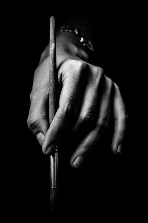 The artist's hands hold a brush. On a black background with deep shadows and bright highlights. Black and white conceptual imageの写真素材