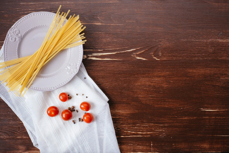 Ingredients for pasta on a wooden table. Plate, cutlery, pasta and fresh vegetables top viewの写真素材