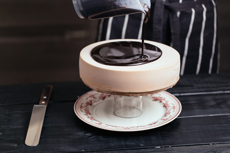 Glazing chocolate mousse cake, close-up. On a wooden table. Liquid chocolate coating