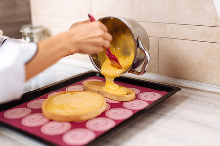 The confectioner fills the lemon pie with stuffing. The pie lies on the red silicone mat in the baking sheet.の写真素材