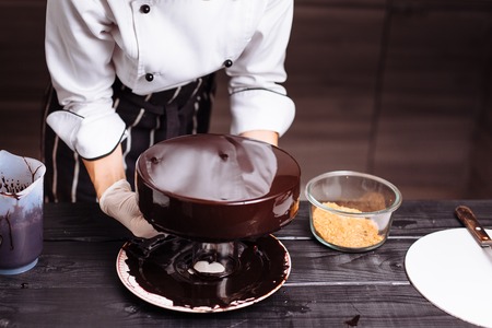Glaze chocolate cake. The confectioner is a young woman, glazes a cake and garnishes it with gold.の写真素材