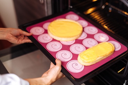 The confectioner puts the biscuit into the oven. On a red silicone sheet. Two forms.