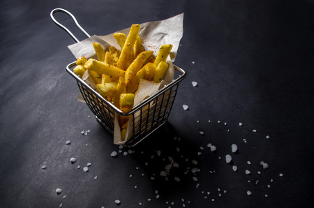 French fries in a basket with salts on black background