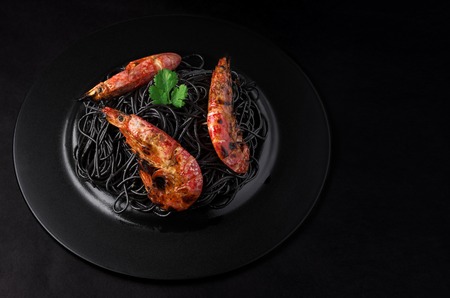 Black spaghetti with shrimps on a black plate and black background with copy space.の写真素材
