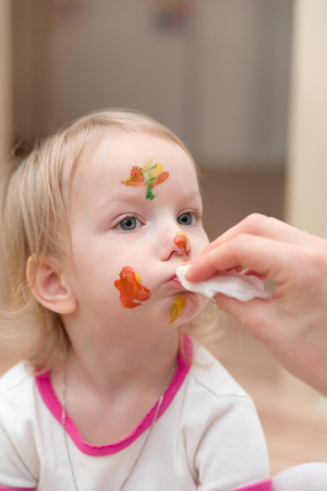 portrait of a little girl smeared with paint, mothers hand wipes cloth face girlの写真素材