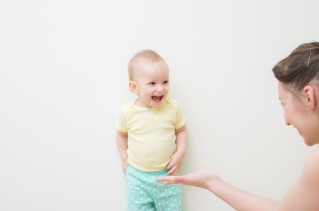 Beautiful young woman and her little daughter smiling while lying in bed at home.Mom stretches out his hand to his daughter, the baby hides his hands.の写真素材