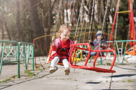 A little girl in a red dress is riding a carousel, a swing ride circuit. At a fun fair.の写真素材